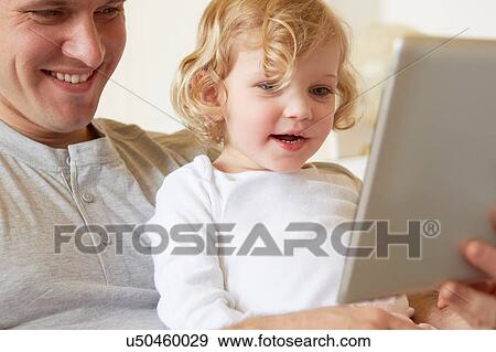 Female toddler sitting on father's knee using digital tablet View Large Photo Image Stock Photo - Female toddler sitting on father's knee using digital tablet. Fotosearch