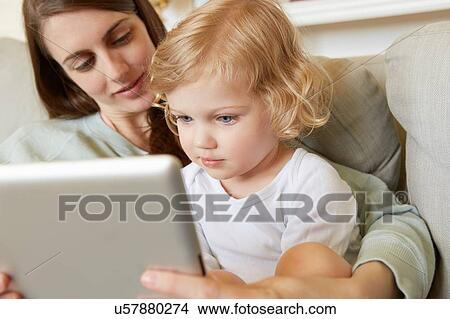 Female toddler sitting on mother's knee looking at digital tablet View Large Photo Image Picture - Female toddler sitting on mother's knee looking at digital tablet. Fotosearch