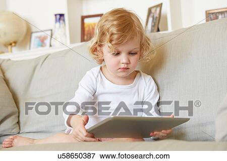 Female toddler sitting on sofa using digital tablet View Large Photo Image Stock Photo - Female toddler sitting on sofa using digital tablet. Fotosearch