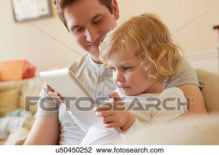 Female toddler sitting on sofa with father using digital tablet View Large Photo Image Stock Image - Female toddler sitting on sofa with father using digital tablet. Fotosearch
