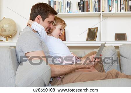Female toddler sitting on sofa with father looking at digital tablet View Large Photo Image Stock Photo - Female toddler sitting on sofa with father looking at digital tablet. Fotosearch