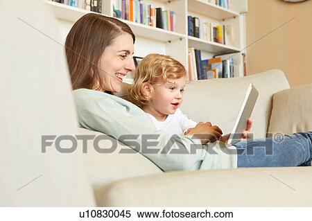 Female toddler sitting on sofa with mother looking at digital tablet View Large Photo Image Stock Photography - Female toddler sitting on sofa with mother looking at digital tablet. Fotosearch