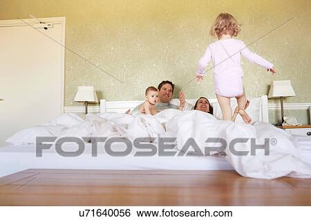 Stock Photograph - Female toddler stepping on bed with parents and baby sister. Fotosearch