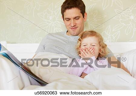 Stock Image - Female toddler yawning in bed with father. Fotosearch