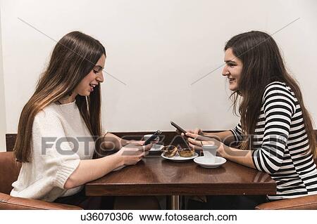 Friends at table in cafe texting on smartphones View Large Photo Image Stock Photograph - Friends at table in cafe texting on smartphones. Fotosearch