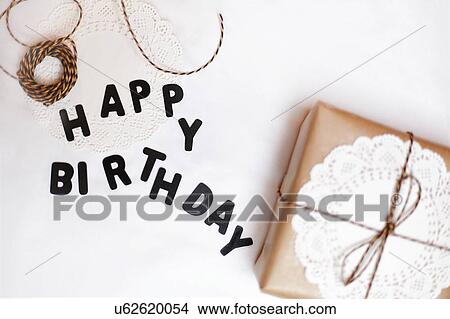 Picture - Gift wrapped in brown paper, doily and string, beside letters spelling Happy Birthday. Fotosearch