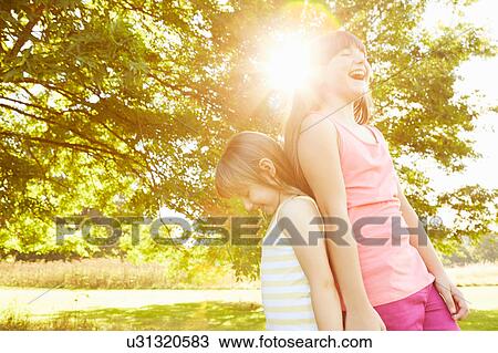 Stock Image - Girl and big sister back to back in park. Fotosearch