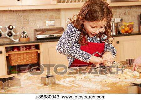 Stock Image - Girl baking star shape pastry at kitchen table. Fotosearch