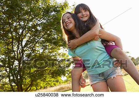 Stock Photo - Girl giving her best friend a piggy back in park. Fotosearch