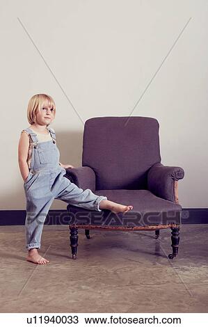 Girl in dungarees with leg raised on vintage armchair View Large Photo Image Stock Image - Girl in dungarees with leg raised on vintage armchair. Fotosearch