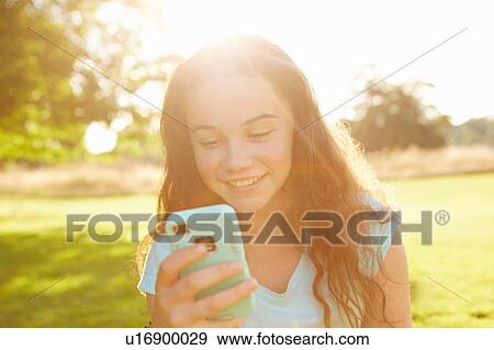 Stock Photo - Girl looking at smartphone in sunlit park. Fotosearch