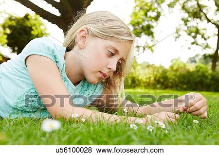 Girl lying on grass gazing at daisy View Large Photo Image Stock Photo - Girl lying on grass gazing at daisy. Fotosearch