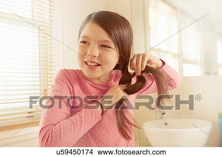 Picture - Girl plaiting long brown hair in bathroom. Fotosearch