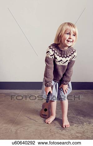 Stock Image - Girl playing with old wooden toy guitar. Fotosearch