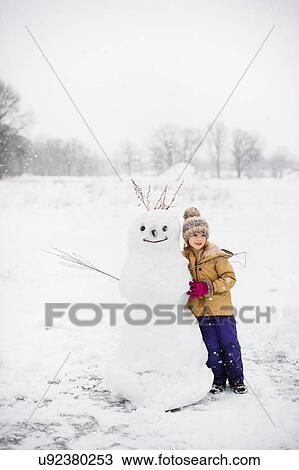Stock Image - Girl shovelling snow in front of snowman, Lakefield, Ontario, Canada. Fotosearch