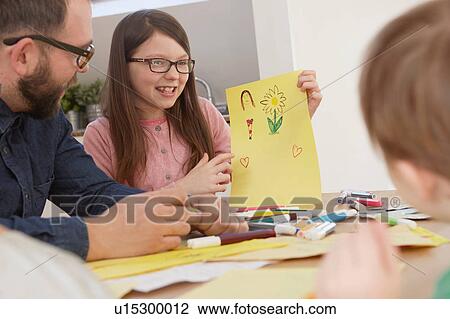 Stock Image - Girl showing brother drawing at table. Fotosearch