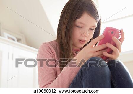 Stock Image - Girl sitting looking at smartphone. Fotosearch