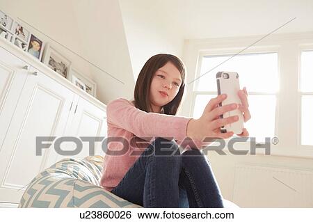Stock Photograph - Girl sitting on beanbag chair taking smartphone selfie. Fotosearch