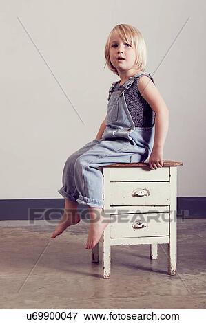Stock Photo - Girl sitting on old cabinet looking away. Fotosearch