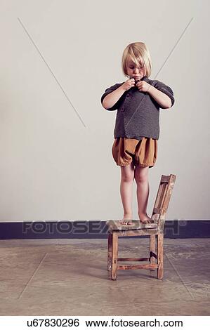 Stock Photograph - Girl standing on old wooden chair fastening cardigan button. Fotosearch