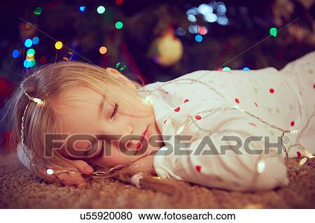 Stock Image - Girl wearing lights asleep on floor at christmas. Fotosearch