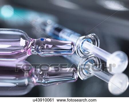 Stock Image - Glass vial of medicine and syringe on surgical tray, close-up. Fotosearch