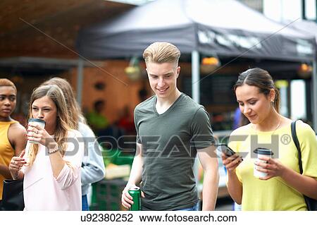 Group of friends, walking outdoors, carrying drinks, looking at smartphone View Large Photo Image Stock Image - Group of friends, walking outdoors, carrying drinks, looking at smartphone. Fotosearch