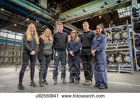 Stock Image - Group portrait of male and female apprentices in car factory. Fotosearch