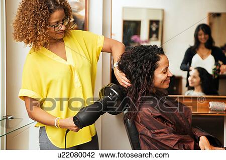 Stock Image - Hairdresser blow drying female customer's hair in hair salon. Fotosearch