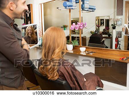 Stock Photograph - Hairdresser showing customer styled long red hair in salon. Fotosearch