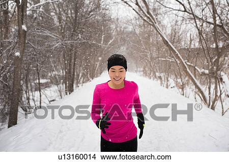 Happy young female runner in knit hat running in snow covered tree lined park View Large Photo Image Picture - Happy young female runner in knit hat running in snow covered tree lined park. Fotosearch