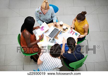 Stock Photo - High angle view of business women sitting at table in meeting. Fotosearch