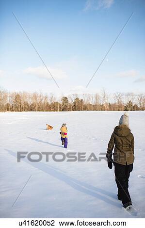 Stock Image - Kids and dogs playing in snow-covered field, Lakefield, Ontario, Canada. Fotosearch
