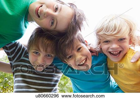 Stock Photograph - Low angle view of four boys with arms around each other in park. Fotosearch