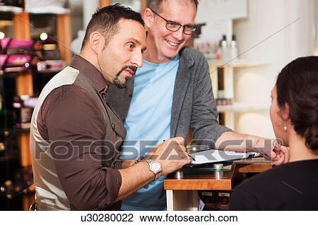 Stock Image - Male hairdressers advising customer on hairstyle in salon. Fotosearch