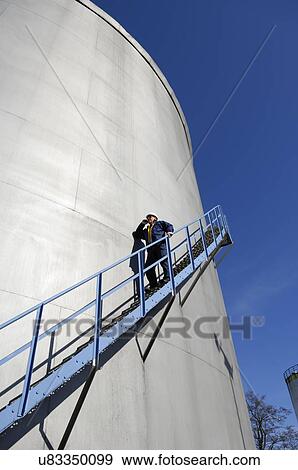 Stock Photo - Man walking down steps on oil storage tower. Fotosearch