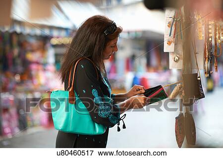 Stock Photo - Mature female tourist looking beaded purse on market stall, Sharjah, United Arab Emirates. Fotosearch