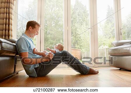 Mature man sitting on floor with baby son on his lap View Large Photo Image Stock Photo - Mature man sitting on floor with baby son on his lap. Fotosearch