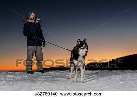 Mature man standing with dog in snow at night View Large Photo Image Stock Image - Mature man standing with dog in snow at night. Fotosearch