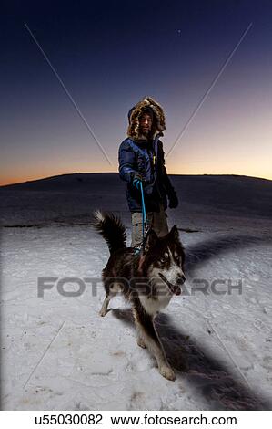 Stock Image - Mature man walking dog in snow at night. Fotosearch