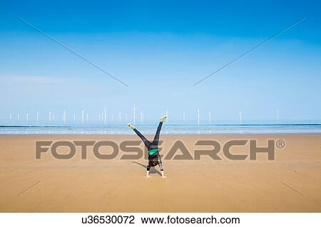 Stock Image - Mature woman doing cartwheel on Redcar beach, North Yorkshire, UK. Fotosearch