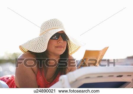 Stock Image - Mature woman lying on pool side lounger reading guidebook, Dubai, United Arab Emirates. Fotosearch