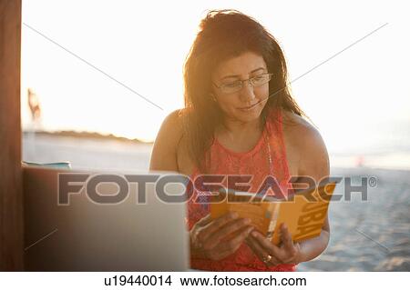 Picture - Mature woman on beach reading guide book, Dubai, United Arab Emirates. Fotosearch