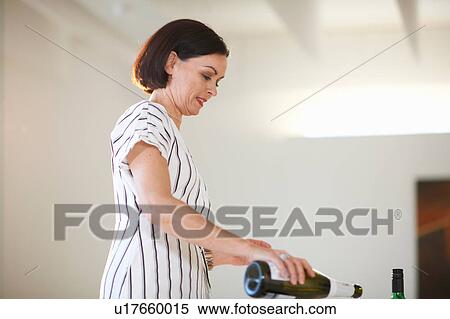Stock Photography - Mature woman pouring white wine at art gallery opening. Fotosearch