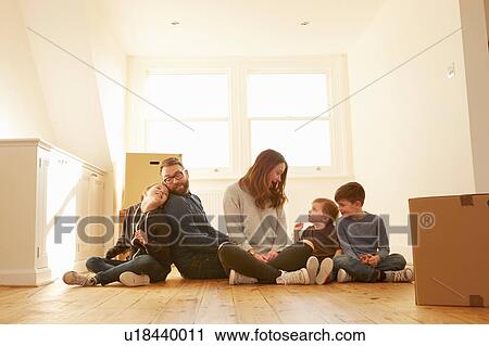 Stock Image - Mid adult couple and three children sitting on floor in new home. Fotosearch