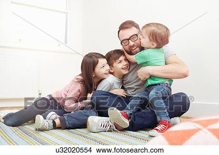 Mid adult man and three children sitting on floor hugging each other View Large Photo Image Picture - Mid adult man and three children sitting on floor hugging each other. Fotosearch