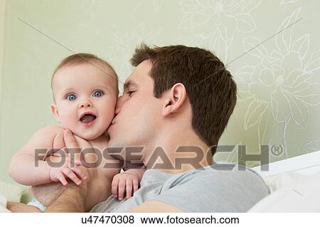 Mid adult man kissing baby daughter on cheek in bed View Large Photo Image Stock Photo - Mid adult man kissing baby daughter on cheek in bed. Fotosearch