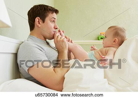 Mid adult man kissing baby daughter's feet in bed View Large Photo Image Picture - Mid adult man kissing baby daughter's feet in bed. Fotosearch