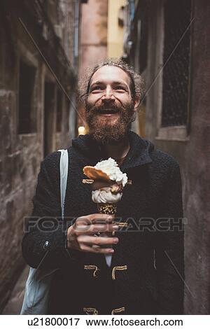 Stock Photo - Mid adult man with gelato in dark alley, Venice, Italy. Fotosearch