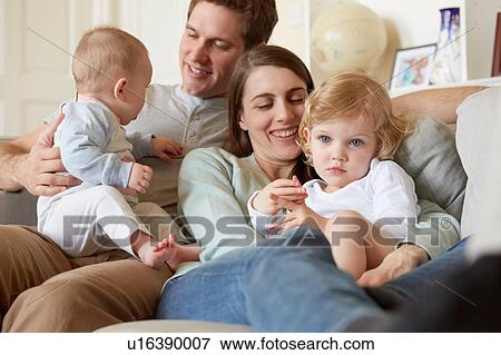 Mid adult parents huddled on sofa with baby and toddler daughter View Large Photo Image Stock Photo - Mid adult parents huddled on sofa with baby and toddler daughter. Fotosearch